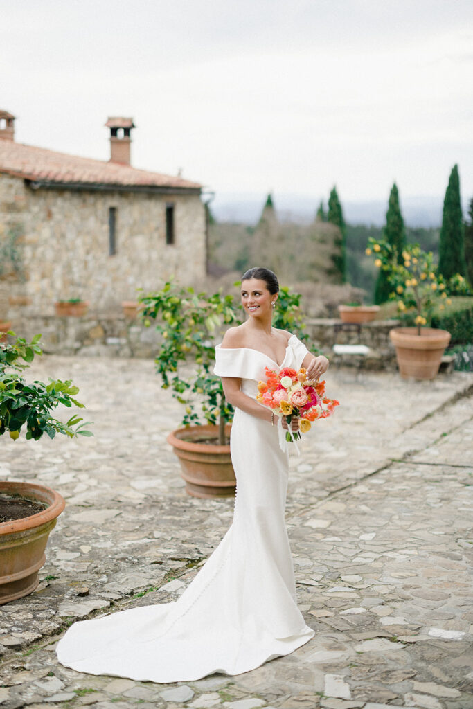 Campbell standing outside at Villa Ardore in Chianti, Tuscany, in her wedding dress holding her bouquet, with vineyards and the Italian countryside surrounding her during her destination wedding.
