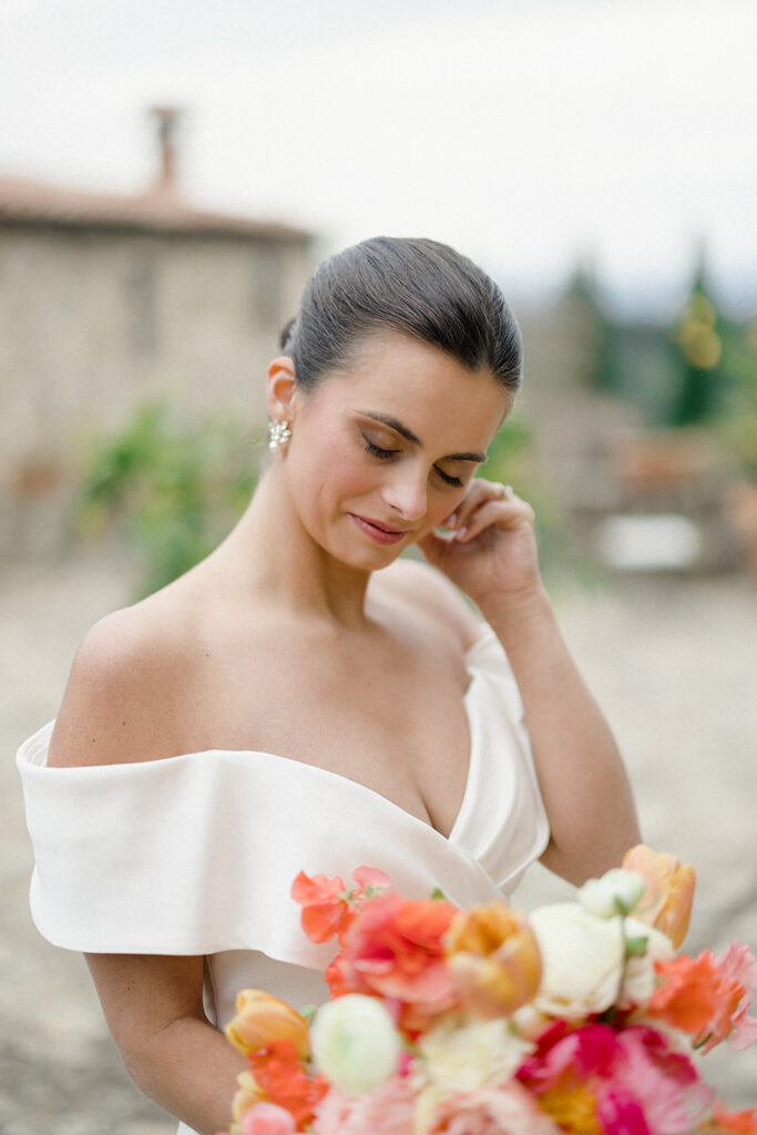 Campbell standing outside at Villa Ardore in Chianti, Tuscany, in her wedding dress holding her bouquet, with vineyards and the Italian countryside surrounding her during her destination wedding.