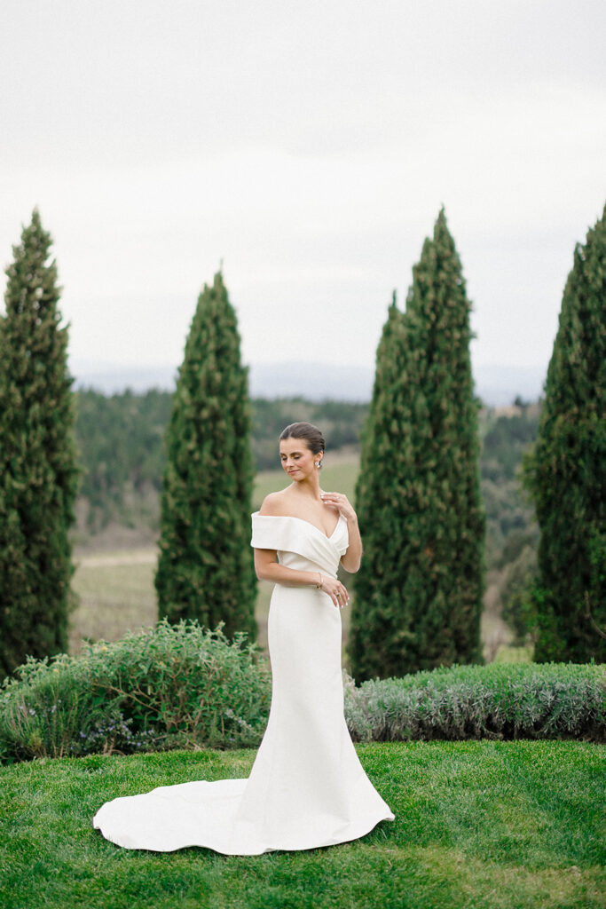 Campbell standing outside at Villa Ardore in Chianti, Tuscany, in her wedding dress holding her bouquet, with vineyards and the Italian countryside surrounding her during her destination wedding.
