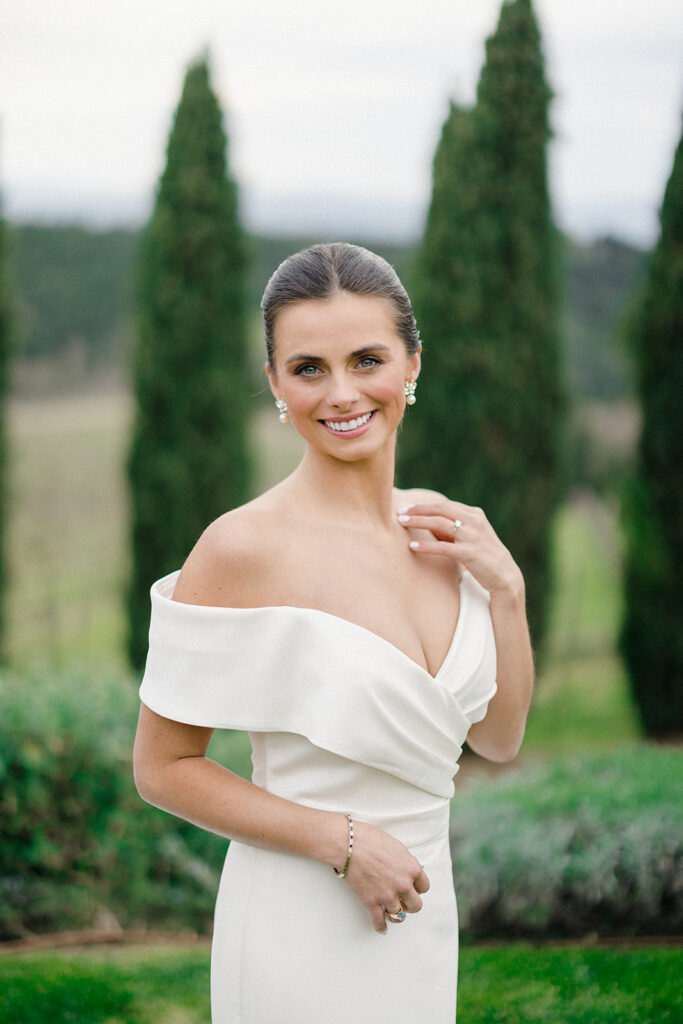Campbell standing outside at Villa Ardore in Chianti, Tuscany, in her wedding dress holding her bouquet, with vineyards and the Italian countryside surrounding her during her destination wedding.