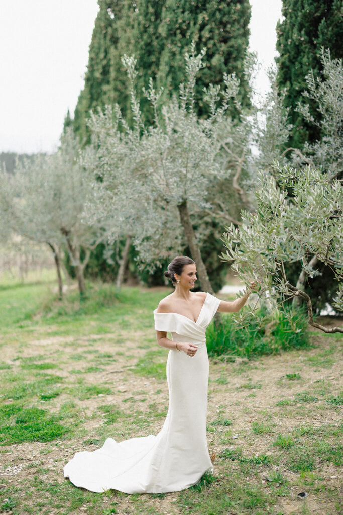 Campbell standing outside at Villa Ardore in Chianti, Tuscany, in her wedding dress holding her bouquet, with vineyards and the Italian countryside surrounding her during her destination wedding.