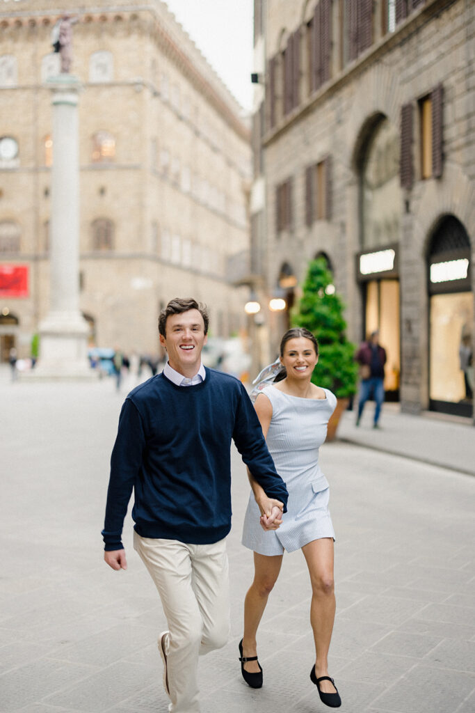 Campbell and Stuart during their engagement session in Florence, Italy, walking through historic cobblestone streets surrounded by classic Renaissance architecture at golden hour before their Tuscany wedding celebration.