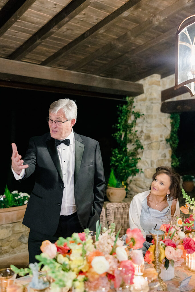 Candlelit wedding reception dinner at Villa Ardore in Chianti, Tuscany, with long tables, vibrant florals by Tuscany Flowers, and family gathered together overlooking the Tuscan hills at sunset.