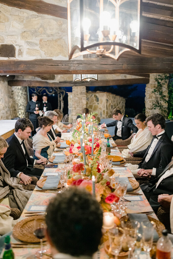 Candlelit wedding reception dinner at Villa Ardore in Chianti, Tuscany, with long tables, vibrant florals by Tuscany Flowers, and family gathered together overlooking the Tuscan hills at sunset.