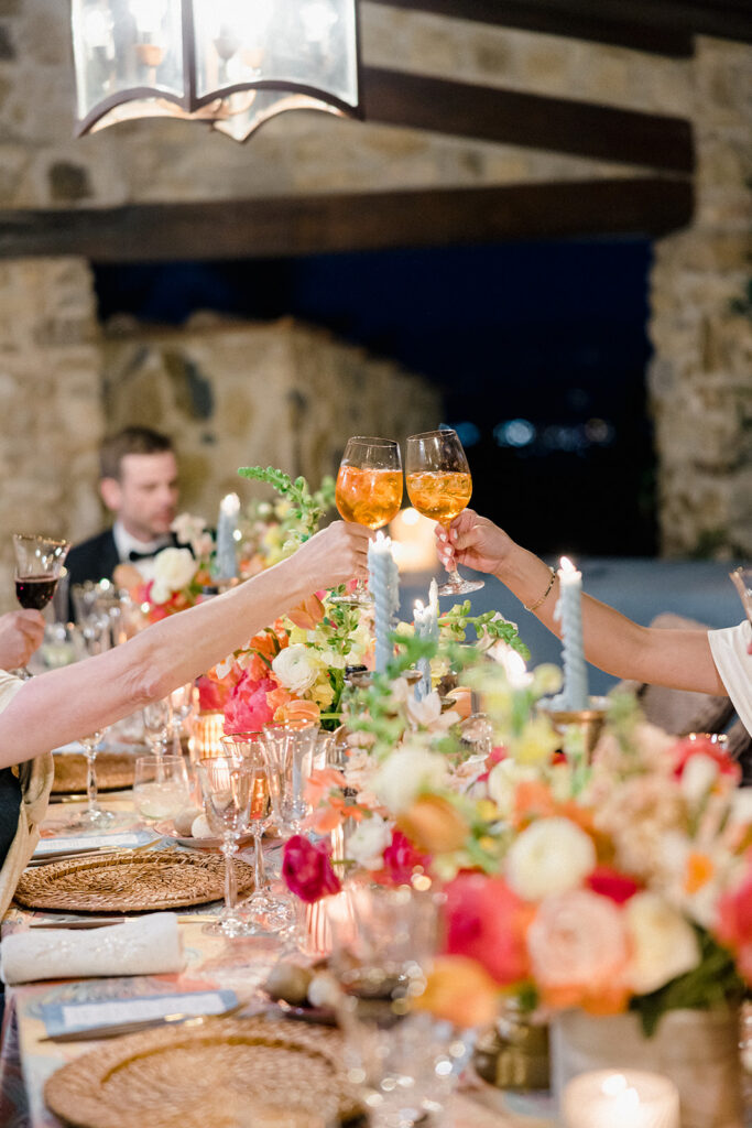 Candlelit wedding reception dinner at Villa Ardore in Chianti, Tuscany, with long tables, vibrant florals by Tuscany Flowers, and family gathered together overlooking the Tuscan hills at sunset.