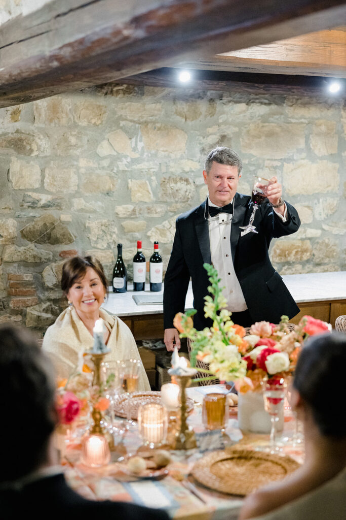 Candlelit wedding reception dinner at Villa Ardore in Chianti, Tuscany, with long tables, vibrant florals by Tuscany Flowers, and family gathered together overlooking the Tuscan hills at sunset.